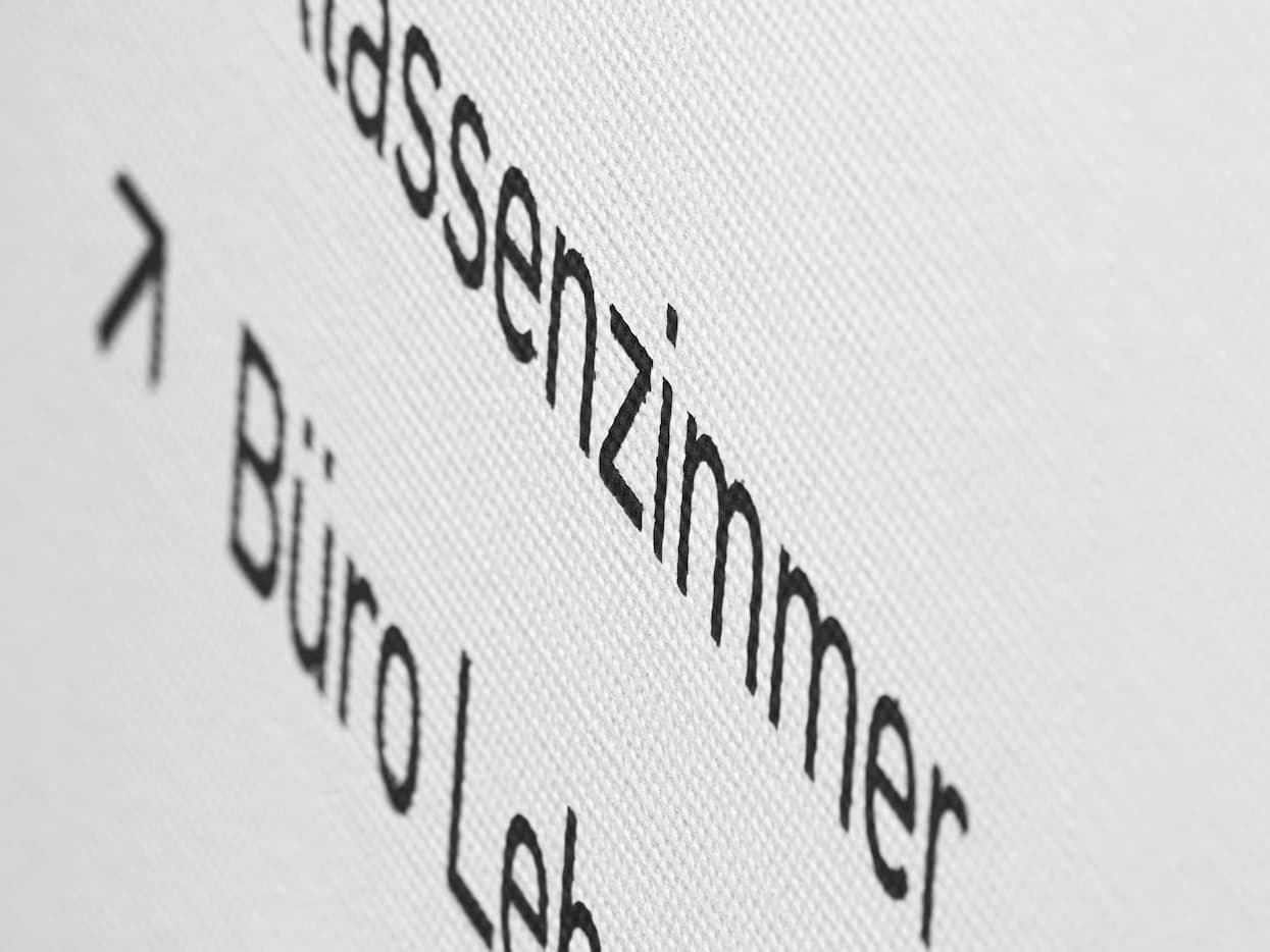 Nahaufnahme der Wegweiser-Beschriftung mit Pfeilen zu «Klassenzimmer» und «Büro»